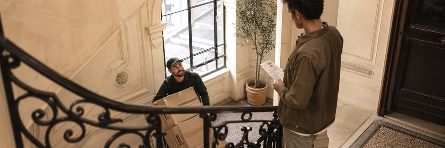 Déménageur manœuvrant un diable dans l'escalier d'un immeuble haussmannien du 11e, client tenant