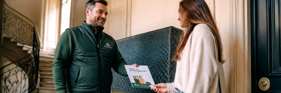 Déménageur remettant une brochure d'aides à une cliente sur un palier haussmannien, meuble protégé