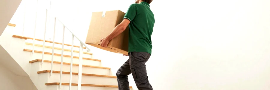 Déménageur en polo vert montant un carton dans l'escalier en bois d'une maison de grande couronne
